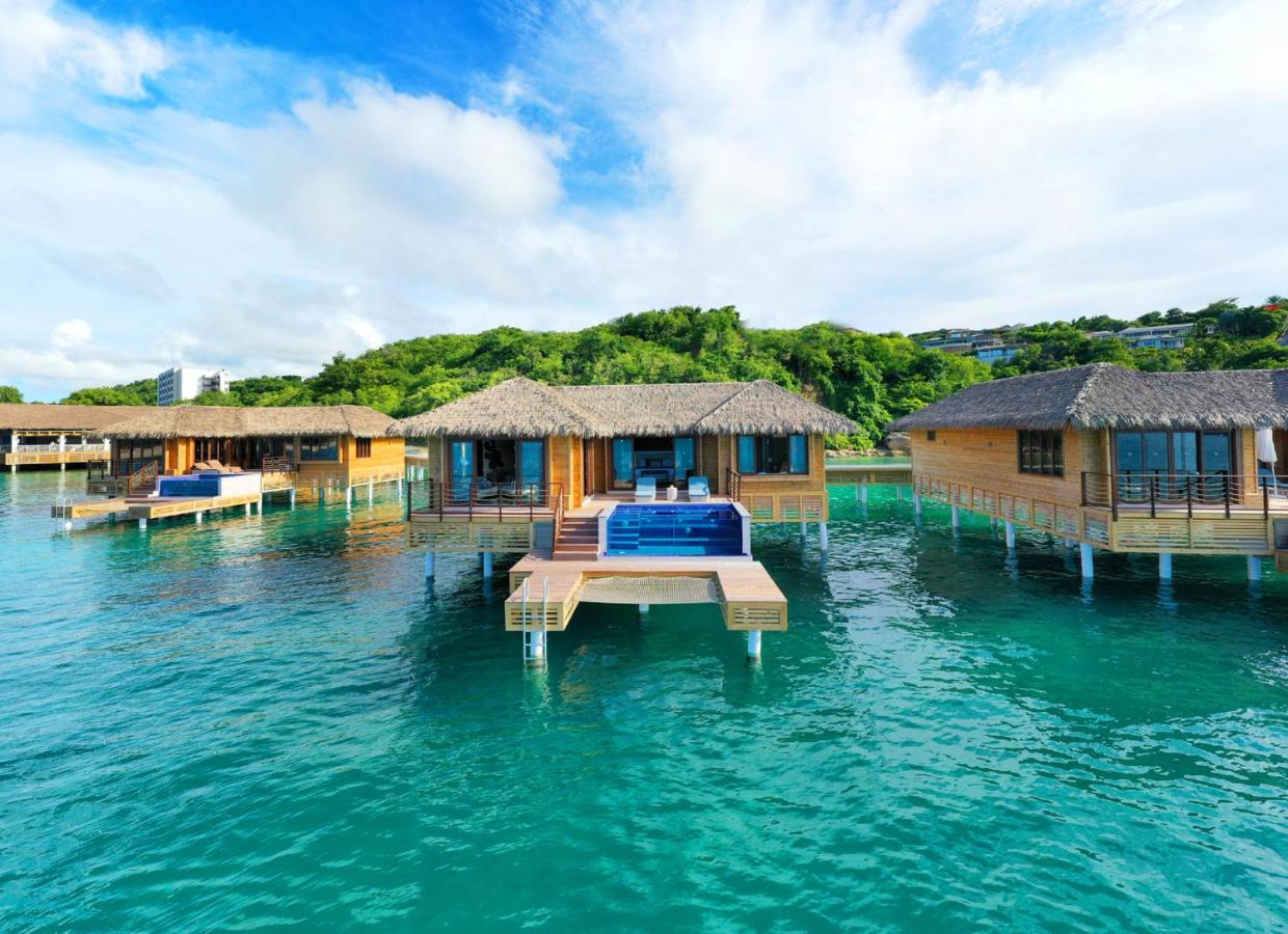 An overwater bungalow with a pool and deck surrounded by turquoise water and trees in the background. 