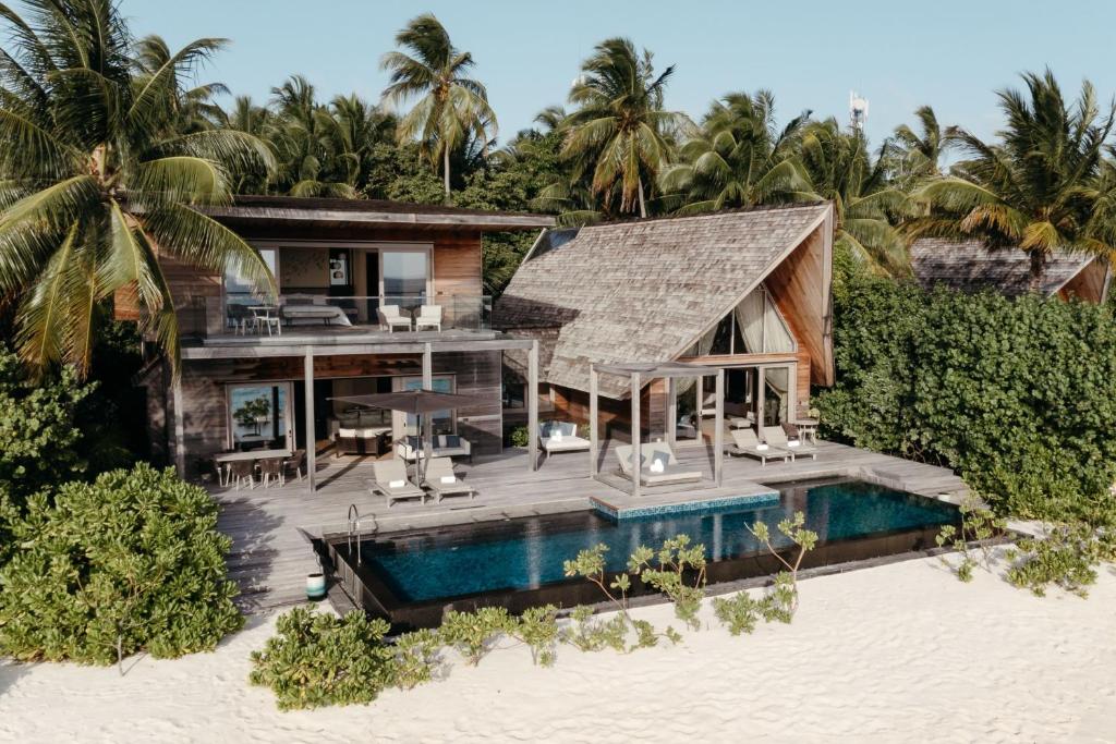 A villa on the beach with its own private pool. There are loungers by the pool and the two story villa is made of wood. 