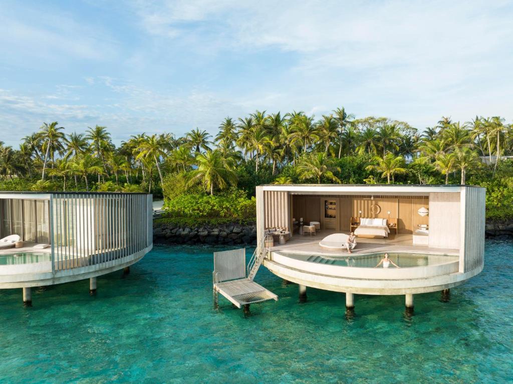 A curved overwater bungalow with a poll outside and palm trees in the background.  