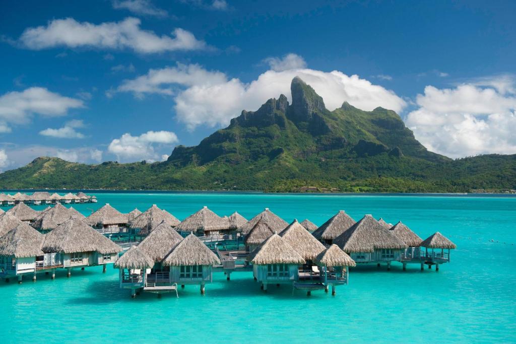 One of the best Marriott hotels in the world. You can see water bungalows with thatched rooves and a mountain in the background. 