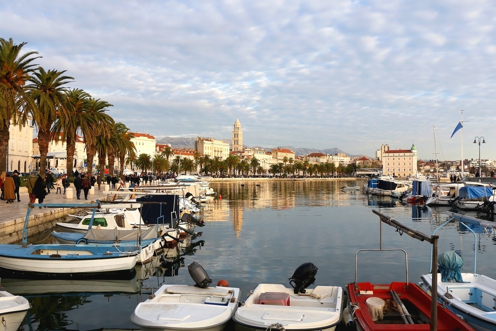 coastal town, buildings along the coast, there are boast parked in the water along the waterside walkway, many clouds in the sky 