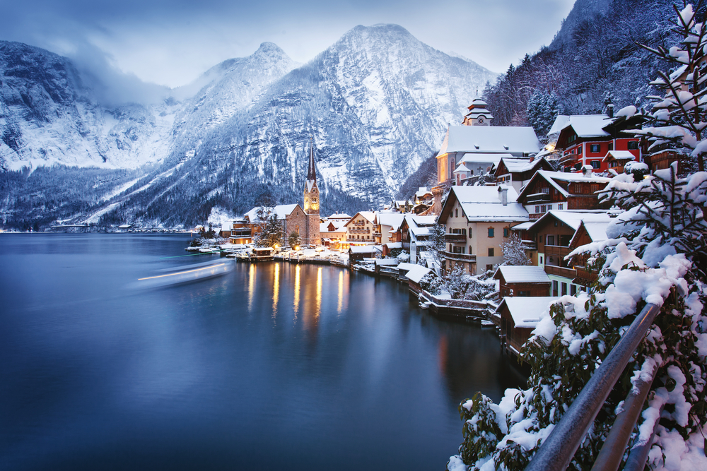 water on the left, buildings on the edge of the water on the right, snow covered mountains are in the background