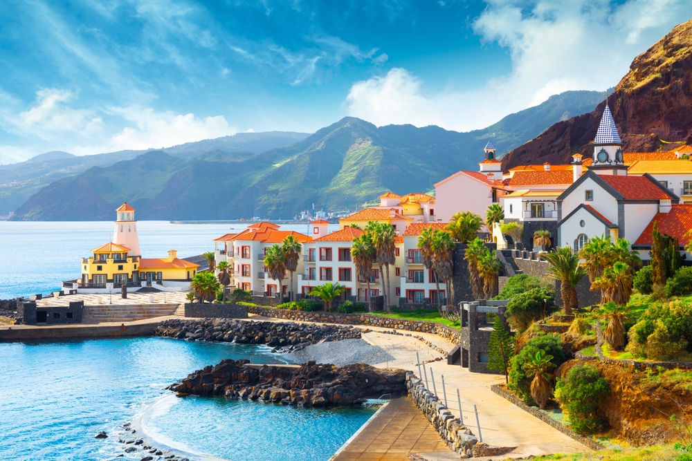 buildings on the coast, water on the left, mountains in the background, palm trees around the buildings 