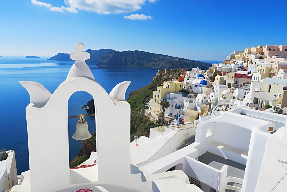 water on the left, ocean mountains in the background, an white hillside buildings on the right on a mostly clear day in santorini, one of the best places to visit in europe in decmber
