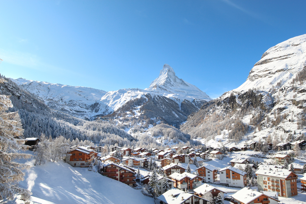 snow covered mountains in switzerland with a village in between them, snow is on the roofs of the buildings, the sky is clear 