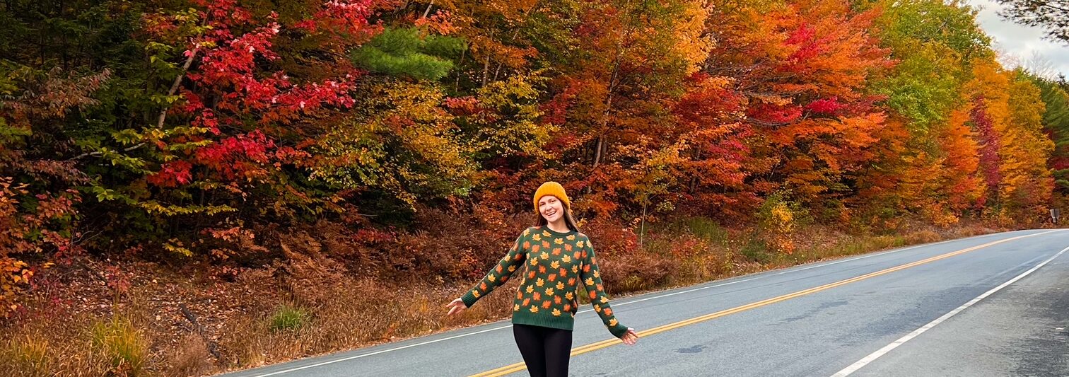 woman standing on a fall foliage lined road