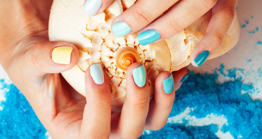 woman wearing nailpolish painted for the beach holding a shell