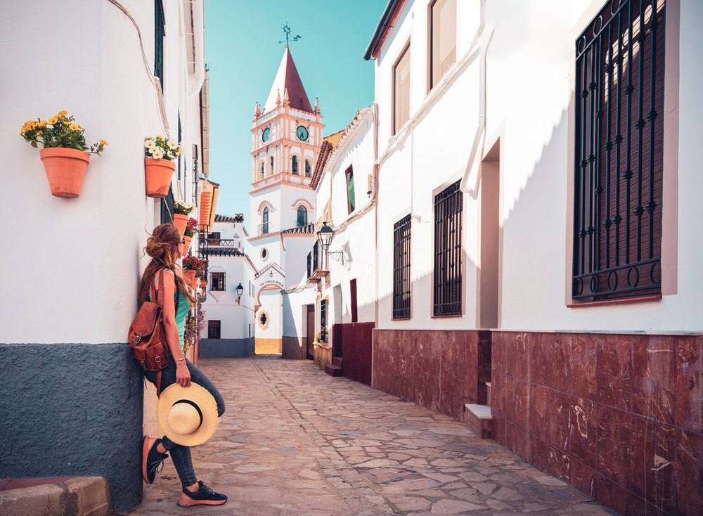 A woman knows what to wear in Spain: as she hides in the cobblestone streets of buildings, she takes off her straw hat and rests with her jeans and tank top in the heat.