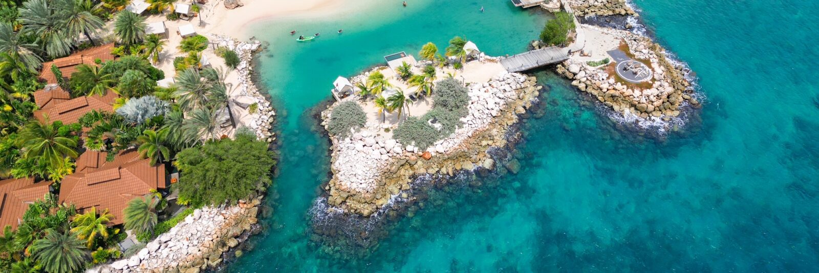 drone view of Baoase luxury resort Curacao which features rocky coastline and buildings with red and orange roofs surrounding a beach in a cove