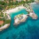 drone view of Baoase luxury resort Curacao which features rocky coastline and buildings with red and orange roofs surrounding a beach in a cove