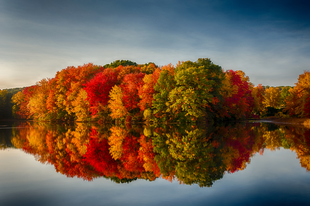 On a lake, the foliage of trees reflect on the glassy water, and you don't want to miss this, as this is one of the mistakes to avoid on a fall foliage trip.