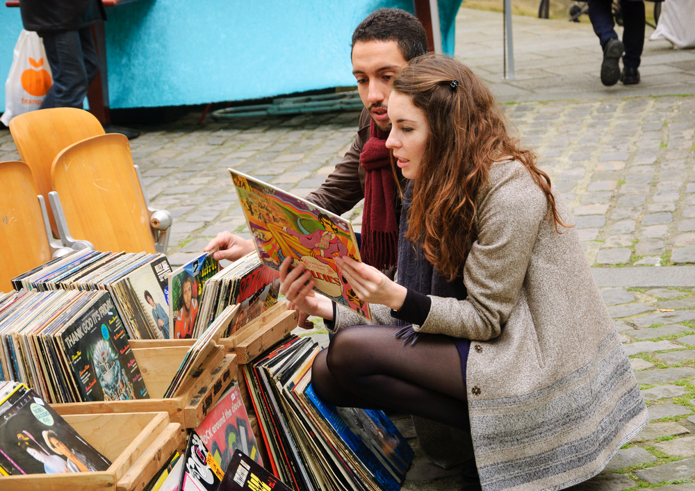 Two friends crouch at a market in Paris, knowing of all mistakes to avoid in Paris includes not falling trap to tourist souvenirs! They brows records.