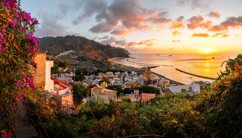 An overhead shot shows the sloping hills and countryside of a town that leads to a beach in Spain at sunset.