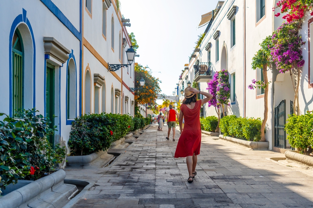 A young woman in a red dress walks down street in Spain, knowing what mistakes to avoid in Spain, enjoying the spring blooms.