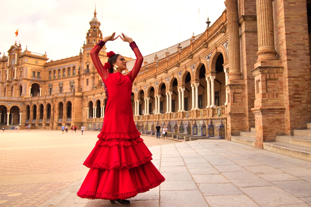 A flamingo dancer in a red dress stretches her arms above her head within an Spanish attraction, standing out!