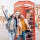 Two girls taking a picture in front of red telephone boxes. one girl is wearing jean jacket and jeans one girl is wearing yellow shirt with jacket and jeans. someones hands are in the picture taking a photo of the two girls. The article is on planning a trip to London.