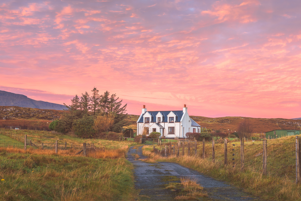 Vibrant, pink colourful sunset or sunrise sky over traditional, rural country croft house in idyllic countryside at Staffin on the Isle of Skye. The article is about Scotland mistakes to avoid.