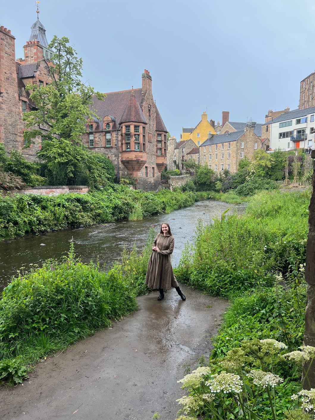 A girl in brown dress posing infant of the iconic Dean's Village pictures near the river, not taking these is one of the mistakes of Avoid in Edinburgh