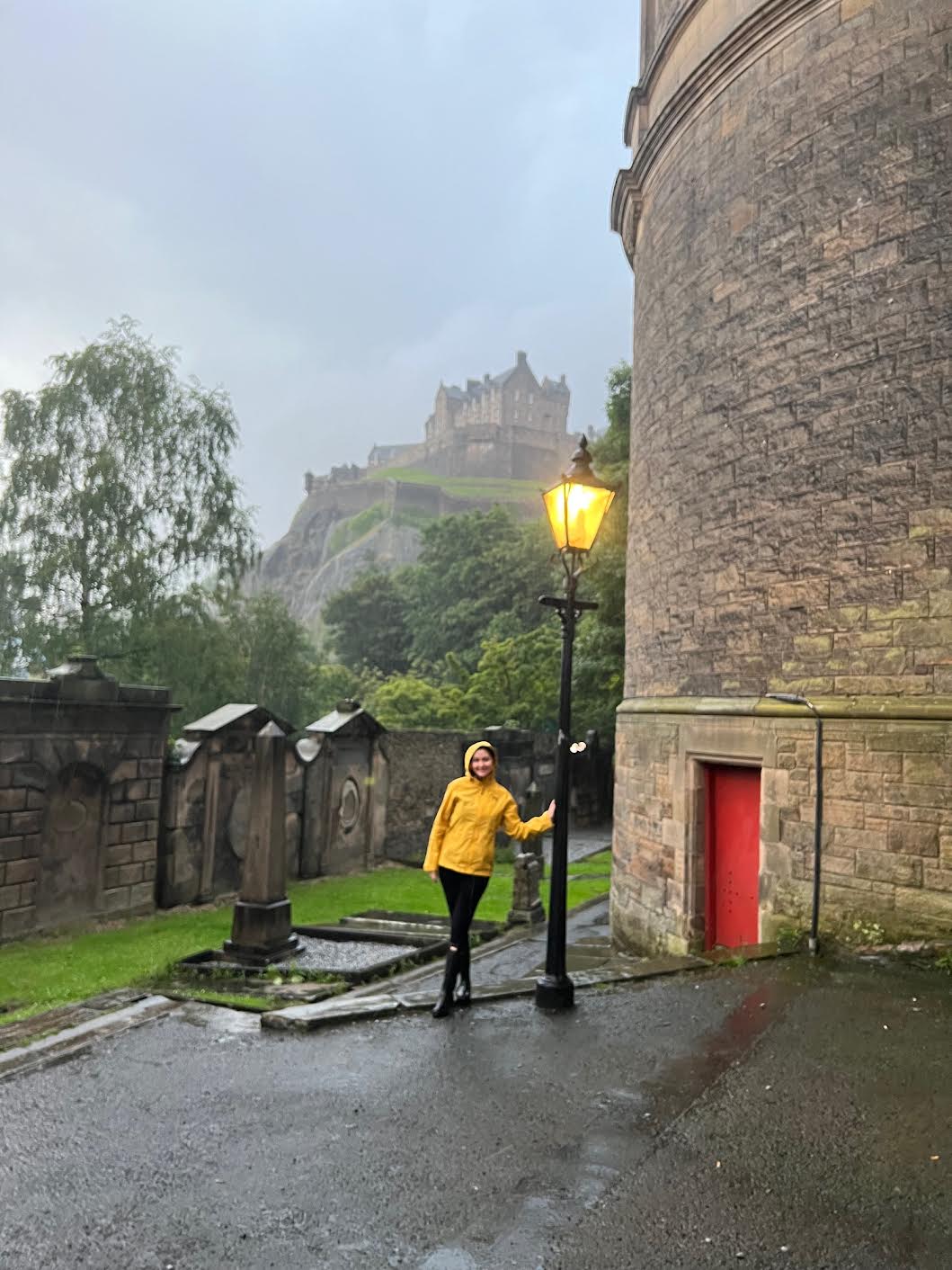 a girl in yellow raincoat leaning against building with the castle in the background