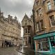 streets of Edinburgh with cobblestone street and brown brick stores. there are people walking outside of the stores. one storefront is green with brown on top with the words "swish" on top of it