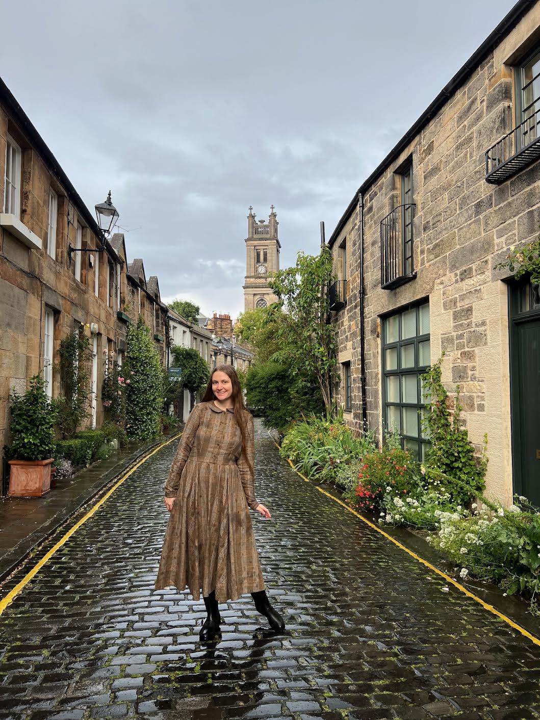 a girl in brown dress standing in Edinburgh in cobblestone streets overlooking the stone buildings learning what mistakes not avoid in Edinburgh