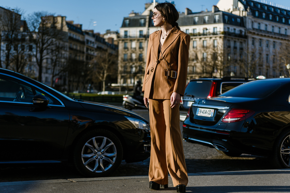 A woman in a matching pants set is stylish in the streets: her tan, leather stands out with her statement jewlery.