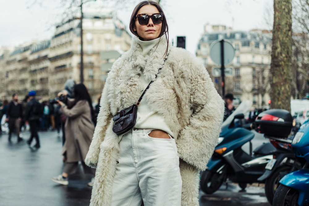 A woman makes a statement with her white jeans, ribbed shirt, crossbody bag, and fur coat: this is What to wear to Paris in November.