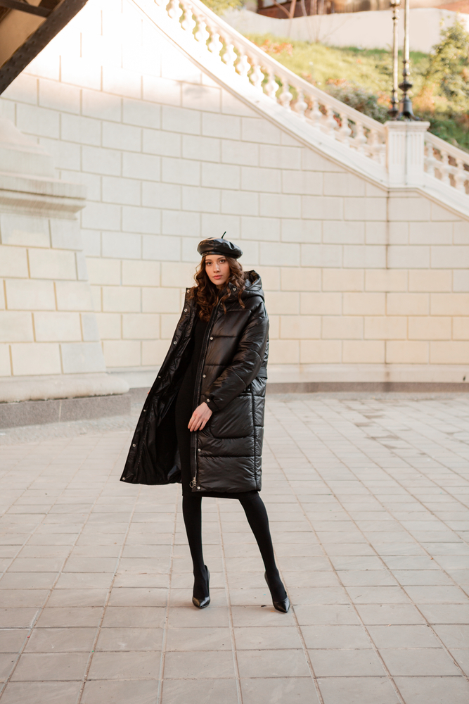 A woman is stylish in a Parisian court yard, wearing a black puffer jacket, leather beret, and all black outfit.