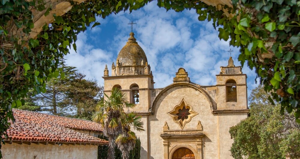 The Spanish Mission inside Carmel by the sea covered archways of ivy with a church in the background and a blue sky with white clouds