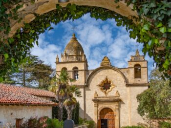 The Spanish Mission inside Carmel by the sea covered archways of ivy with a church in the background and a blue sky with white clouds