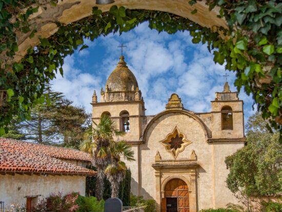 The Spanish Mission inside Carmel by the sea covered archways of ivy with a church in the background and a blue sky with white clouds