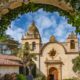 The Spanish Mission inside Carmel by the sea covered archways of ivy with a church in the background and a blue sky with white clouds