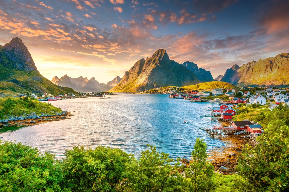 the picturesque town of Reine Norway with lake red homes dot the shorliena nd towering mountains in the background