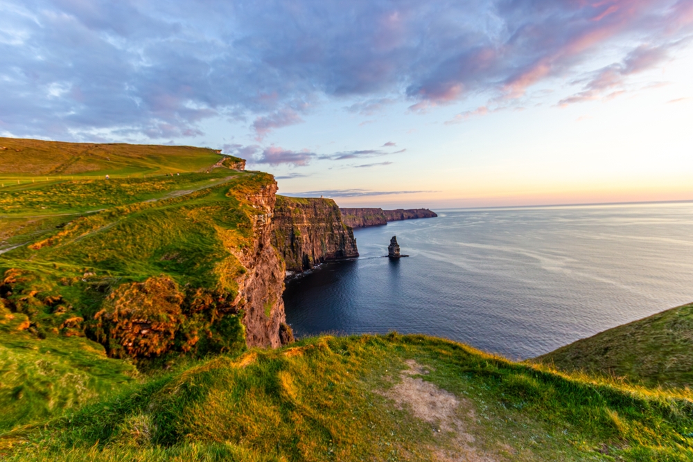 At golden hour, the Cliffs of Moher stand tall and green, their rugged edges cutting into the glassy water: you can see things like this in Ireland when you know what things to buy from Amazon for Europe and are prepared for your trip.
