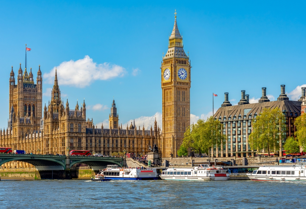 Big Ben stands tall and golden amongst the backdrop of London, the river, and ferries on the water.