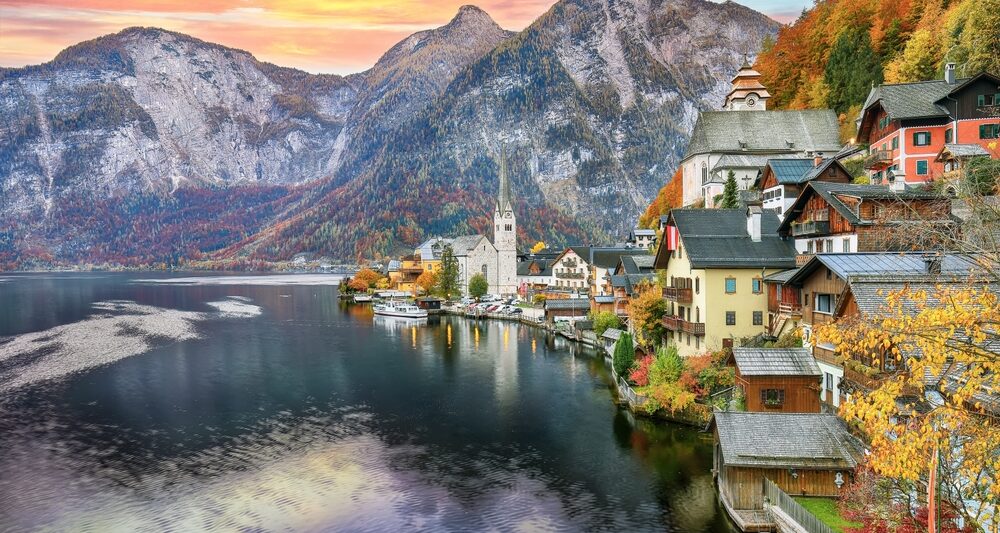 Mountains tower in the sunset of this European town, and the turn of leaves match the autumn hues of the homes on the lack: you can see things like this too if you prepare and know what things to buy from Amazon for Europe.