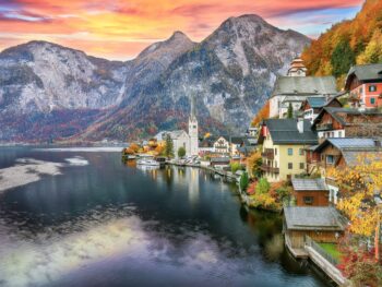 Mountains tower in the sunset of this European town, and the turn of leaves match the autumn hues of the homes on the lack: you can see things like this too if you prepare and know what things to buy from Amazon for Europe.