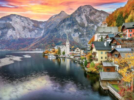 Mountains tower in the sunset of this European town, and the turn of leaves match the autumn hues of the homes on the lack: you can see things like this too if you prepare and know what things to buy from Amazon for Europe.