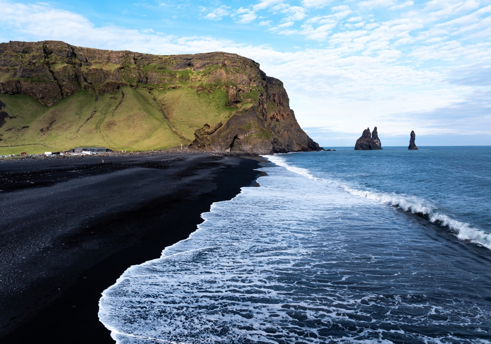 In Iceland, the black stand beaches are dark and contrasted against the icy blue waters and green rugged mountains beyond it.