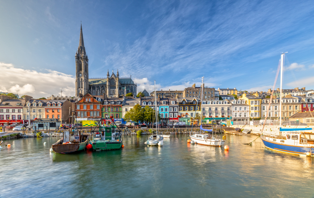 In a city on the coast, boats line the water in the forefront of the photo, and brightly colored tall buildings with tons of Windows are in the middle ground, and churches are in the background: seeing this is possible when you prep for your trip and know which things to buy from Amazon for Ireland