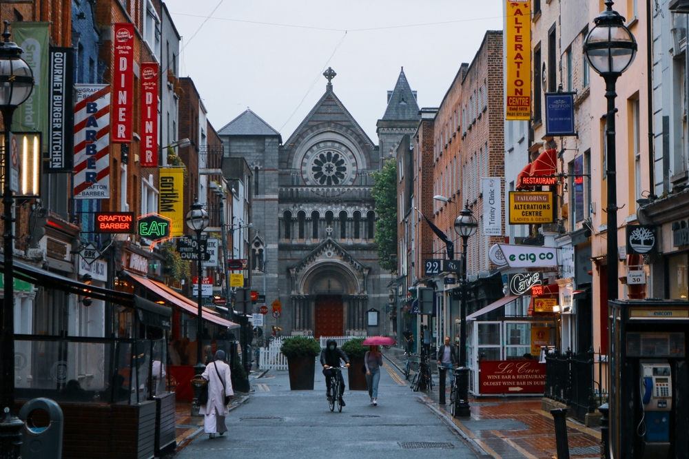 In Dublin, the city is lined with vibrant buildings, and down the street a church stands tall as people walk in the rain: getting things for the rain and other things to buy from Amazon for Ireland prepares you for this!