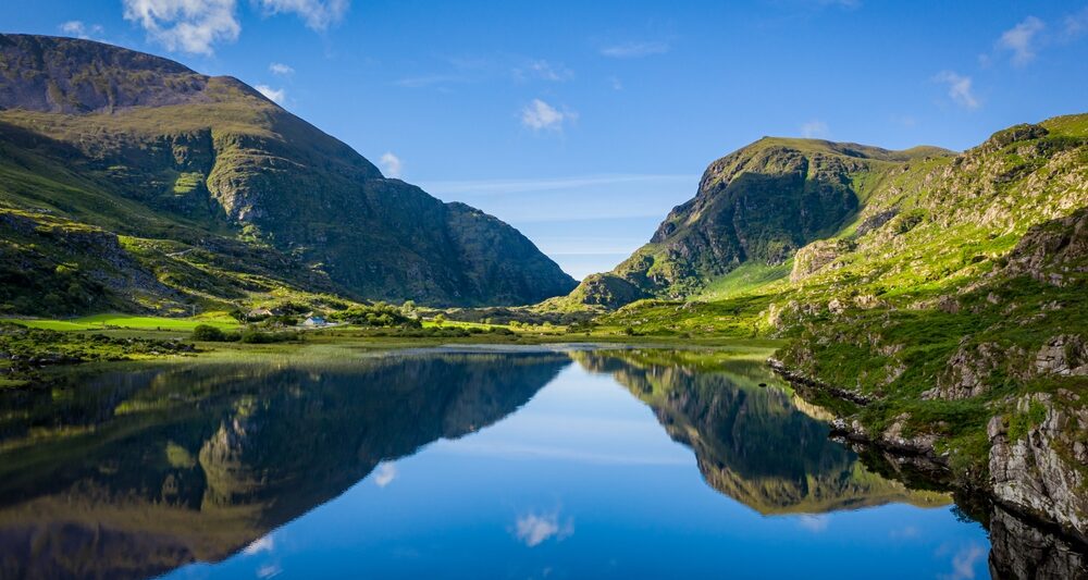 The rolling hills and cliffs of the green land of Ireland come together and reflect over a glassy lake: you can see these stunning views when you prep for your trip and know which things to buy from Amazon for Ireland!