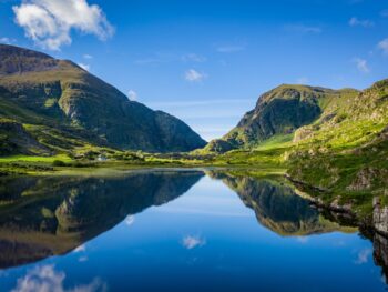 The rolling hills and cliffs of the green land of Ireland come together and reflect over a glassy lake: you can see these stunning views when you prep for your trip and know which things to buy from Amazon for Ireland!