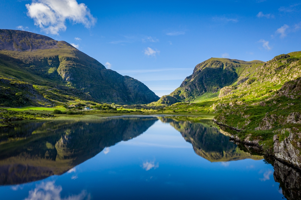 The rolling hills and cliffs of Ireland are vibrant as they stretch before a glassy lake, their reflection strong in the water: you can see things like this too when you know what things to buy from Amazon for Ireland.