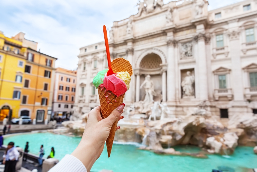 A hand holds up colorful gelato in front of the Trevi Fountain: they knew what things to buy from Amazon for Italy