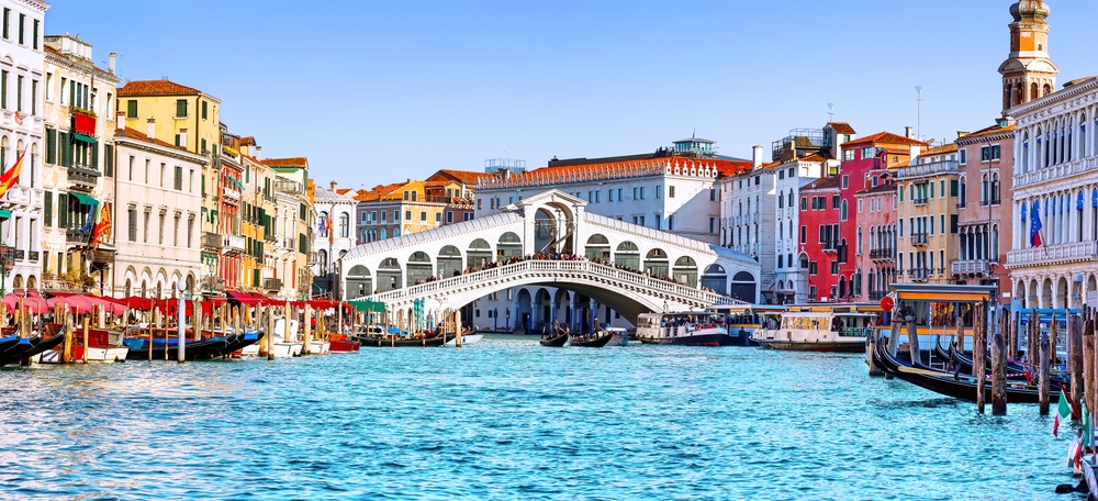 A bridge connects two sides of the a city in Italy, their buildings bright with colors, and the water underneath them smooth. Knowing the things to buy from Amazon for Italy helps explore places like this. 