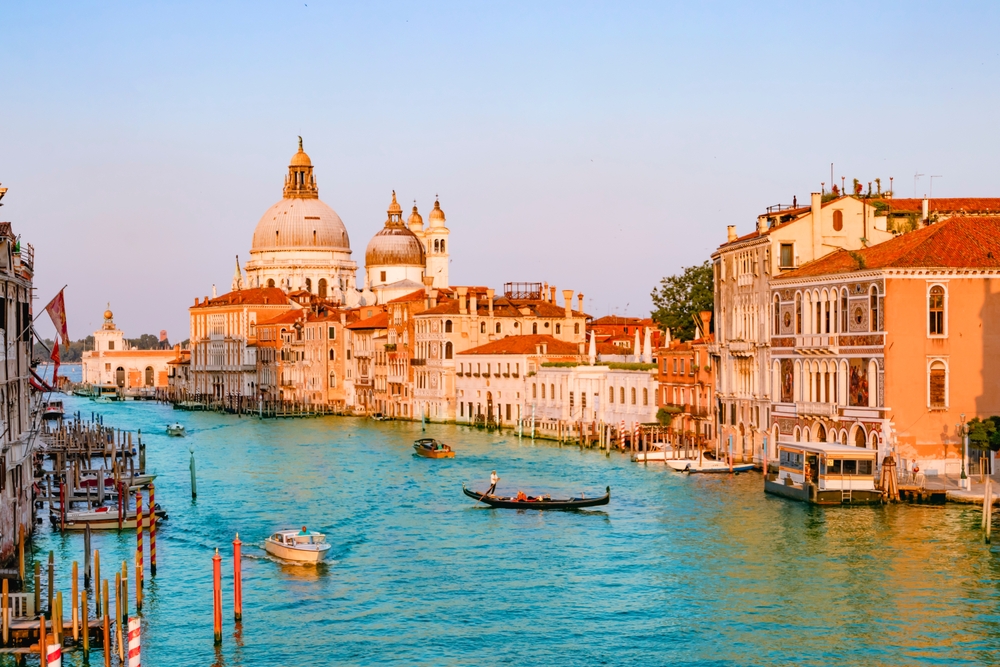 Venice in golden hour shows the buildings aglow and boats going through the water, which is things you can see and do if you know what things to buy from Amazon for Italy.
