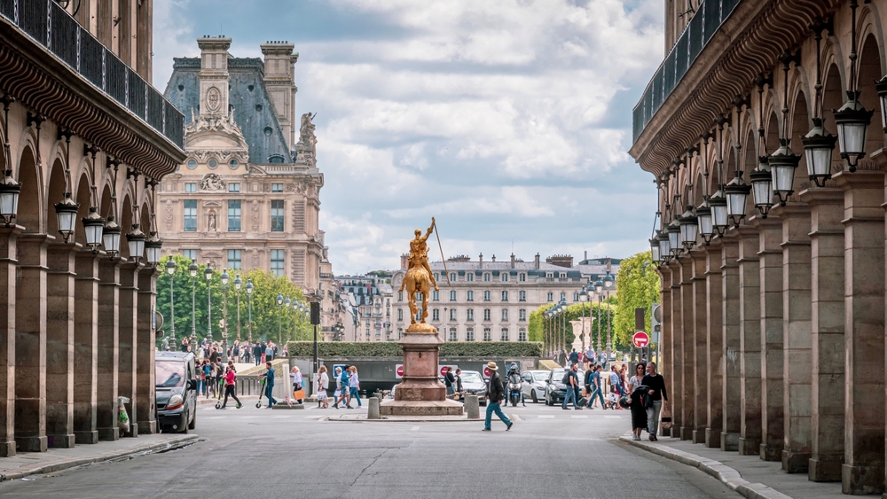 A statue of gold sits in the middle of a square in Paris as people hustle and bustle by.