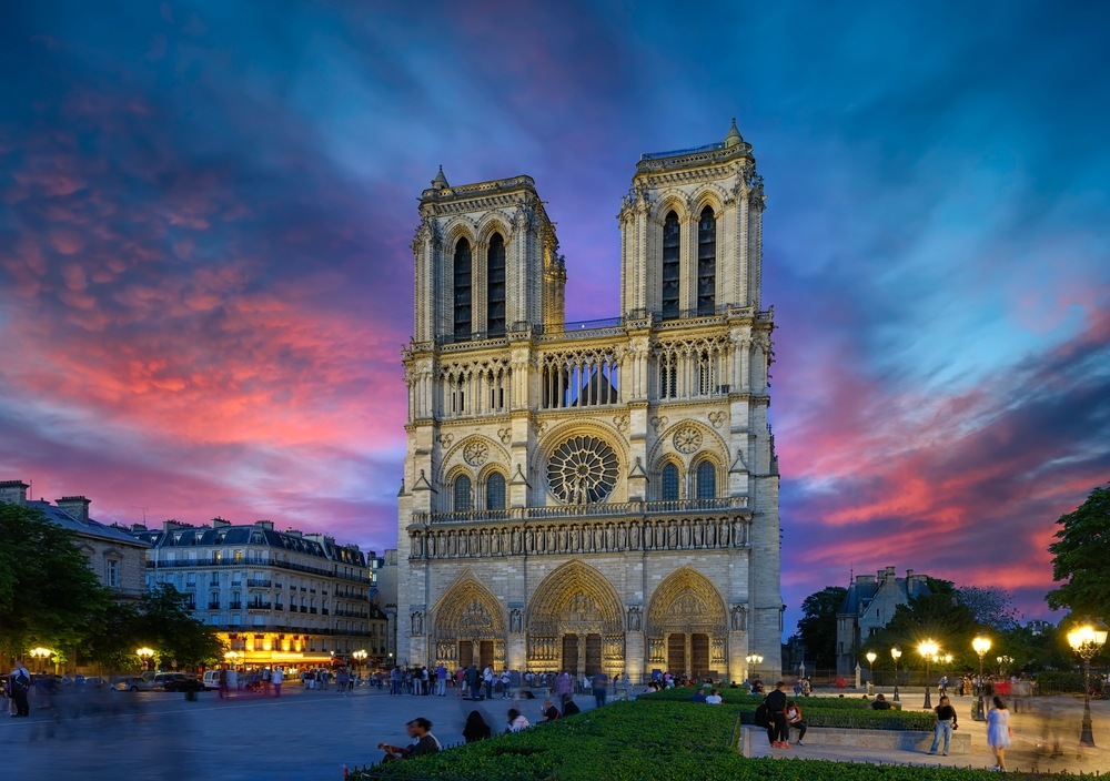 At sunset, with blue and pink clouds beyond, Notre Dame stands tall with its towers and windows before its devastating fire.