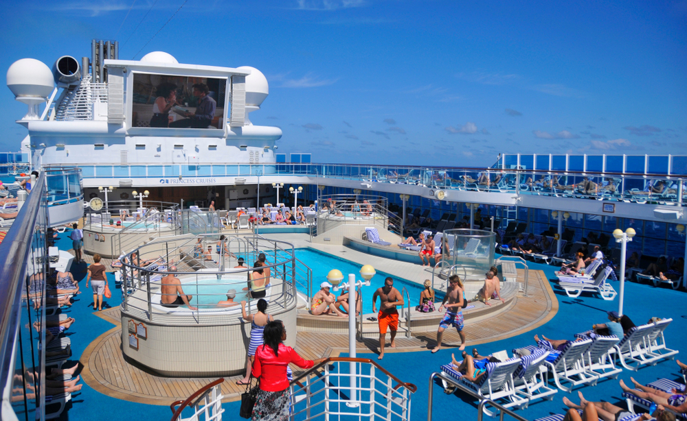 A photo of the deck of the cruise ship shows guests enjoying pools, hot tubs and the sun, all knowing what things to buy from Amazon for a cruise to enjoy this time. 
